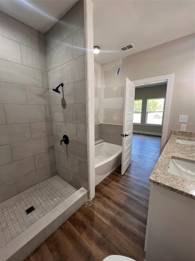 bathroom featuring wood finished floors, visible vents, a bath, double vanity, and a stall shower