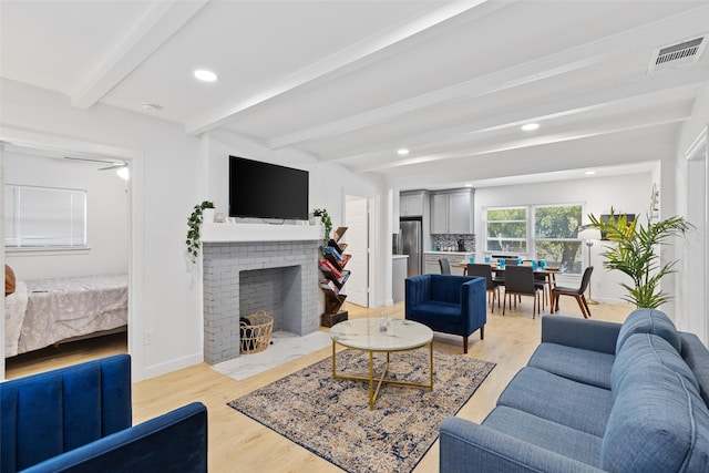 living room with beam ceiling, a brick fireplace, and light hardwood / wood-style flooring