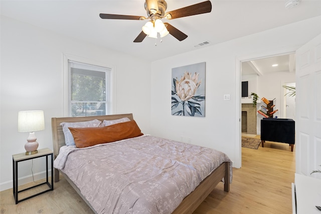 bedroom with ceiling fan, a fireplace, and light hardwood / wood-style flooring