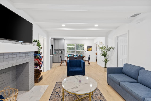 living room featuring beamed ceiling, a brick fireplace, and light hardwood / wood-style flooring