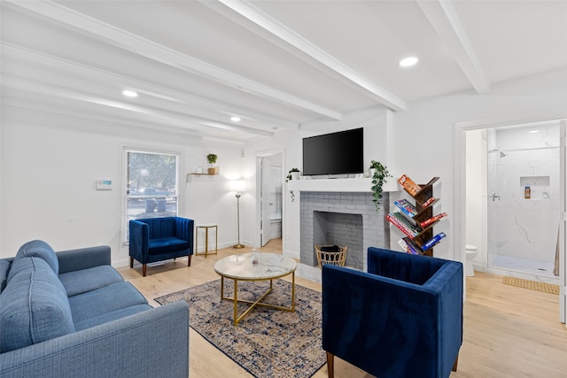 living room featuring beamed ceiling, a fireplace, and light wood-type flooring