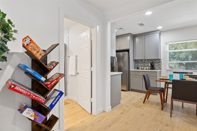 kitchen with stainless steel refrigerator with ice dispenser, light wood-type flooring, decorative backsplash, and gray cabinetry