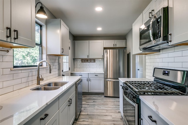 kitchen with sink, tasteful backsplash, light wood-type flooring, appliances with stainless steel finishes, and light stone countertops