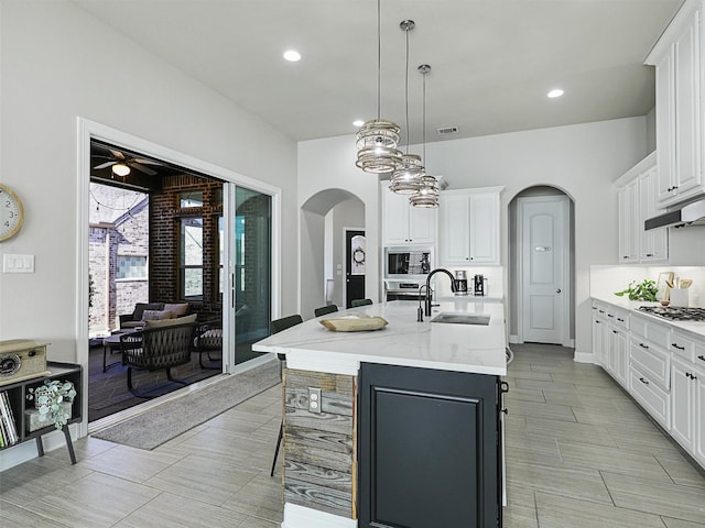 kitchen with sink, white cabinets, hanging light fixtures, a kitchen island with sink, and light stone countertops