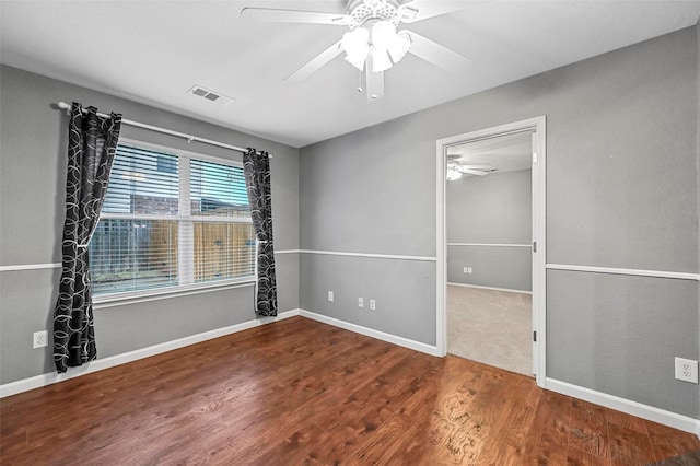 empty room with ceiling fan, wood finished floors, visible vents, and baseboards