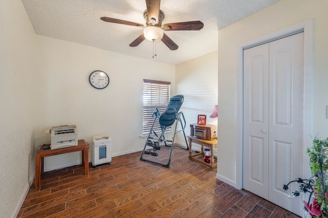 exercise room featuring ceiling fan, dark wood-type flooring, and a textured ceiling