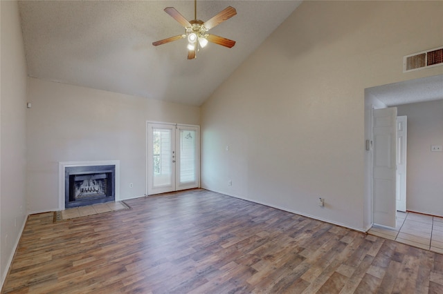 unfurnished living room with high vaulted ceiling, hardwood / wood-style flooring, ceiling fan, a textured ceiling, and french doors