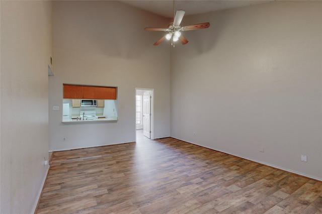 unfurnished living room with a towering ceiling, ceiling fan, and light hardwood / wood-style flooring