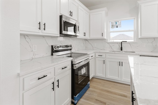 kitchen with light wood-type flooring, a sink, tasteful backsplash, white cabinetry, and appliances with stainless steel finishes