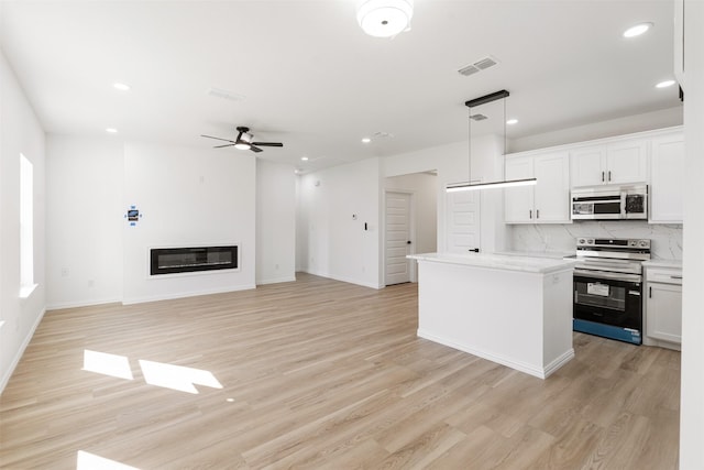 kitchen featuring visible vents, a kitchen island, appliances with stainless steel finishes, a glass covered fireplace, and light wood-type flooring