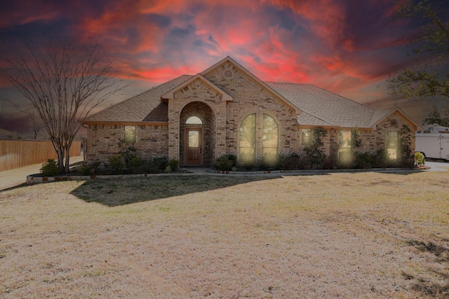 french provincial home with brick siding, a shingled roof, a front yard, and fence