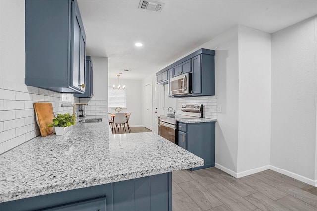 kitchen with sink, blue cabinetry, an inviting chandelier, stainless steel appliances, and kitchen peninsula