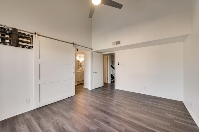 empty room with dark hardwood / wood-style floors, a barn door, ceiling fan, and a high ceiling