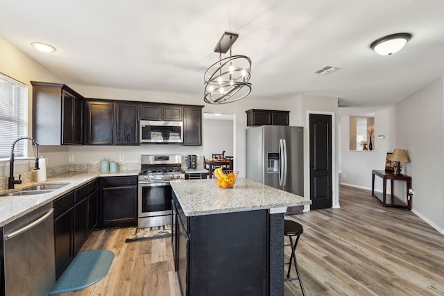 kitchen with sink, appliances with stainless steel finishes, a center island, a kitchen bar, and decorative light fixtures