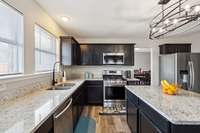 kitchen with pendant lighting, sink, light hardwood / wood-style flooring, stainless steel appliances, and light stone counters