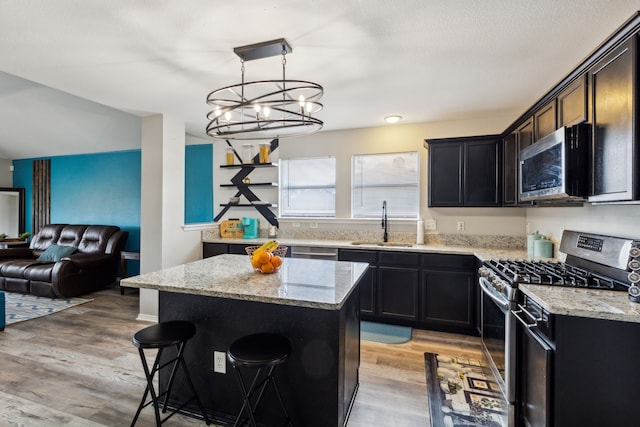 kitchen featuring sink, light stone counters, a center island, hanging light fixtures, and stainless steel appliances