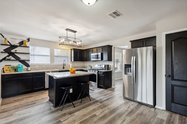 kitchen with a breakfast bar area, appliances with stainless steel finishes, a center island, decorative light fixtures, and light wood-type flooring