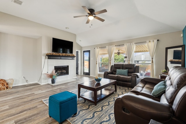 living room with a tile fireplace, vaulted ceiling, wood-type flooring, and ceiling fan