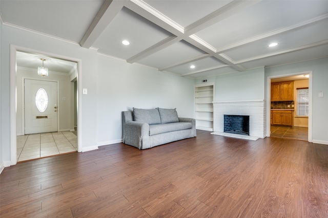 unfurnished living room with crown molding, beam ceiling, coffered ceiling, a brick fireplace, and light wood-type flooring