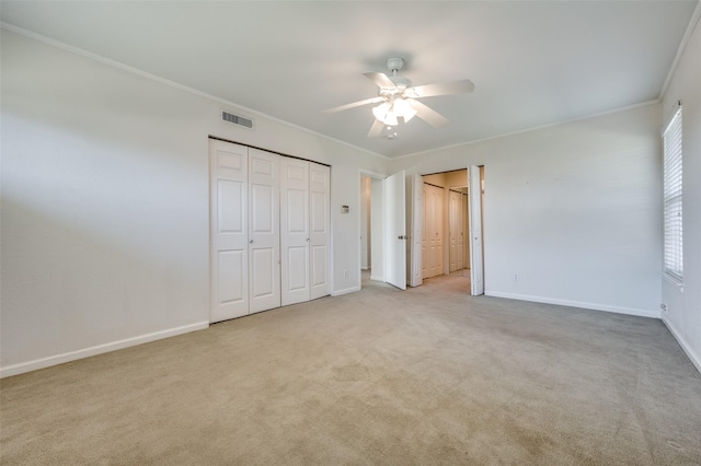 unfurnished bedroom with multiple closets, crown molding, light colored carpet, and ceiling fan