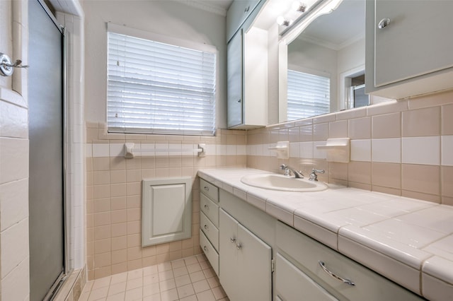 bathroom with tile walls, vanity, ornamental molding, a shower with door, and tile patterned floors