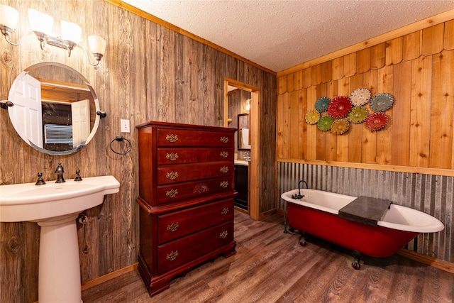 bathroom with sink, hardwood / wood-style flooring, a bathtub, a textured ceiling, and wood walls