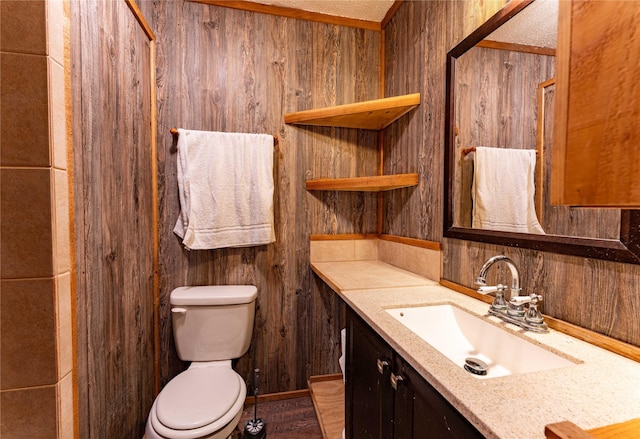 bathroom featuring vanity, toilet, a textured ceiling, and wood walls