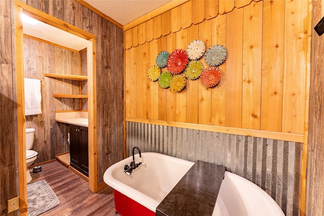 bathroom with wooden walls, a bathtub, hardwood / wood-style flooring, toilet, and a textured ceiling