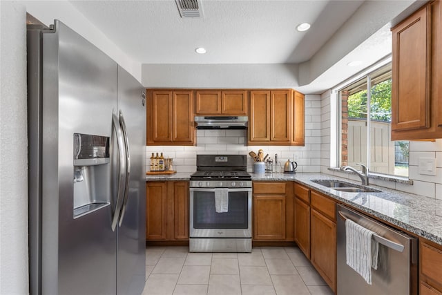 kitchen with light stone counters, stainless steel appliances, sink, and decorative backsplash