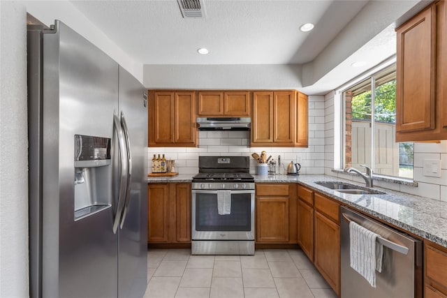 4808 Briarwood Ln, Fort Worth, TX 76103 - kitchen featuring stainless steel appliances, a sink, under cabinet range hood, brown cabinetry, and a textured ceiling