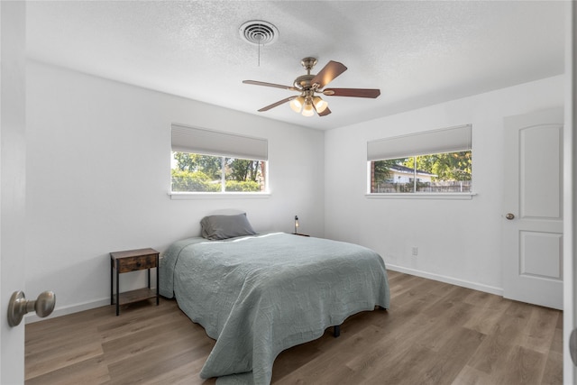 bedroom featuring multiple windows, a textured ceiling, and light hardwood / wood-style flooring