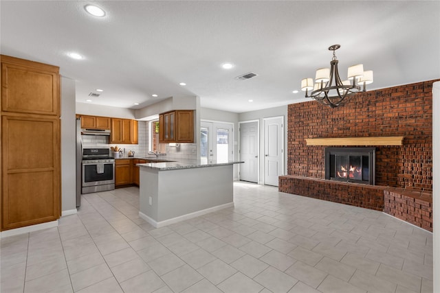 kitchen with pendant lighting, light stone countertops, stainless steel range oven, a brick fireplace, and kitchen peninsula