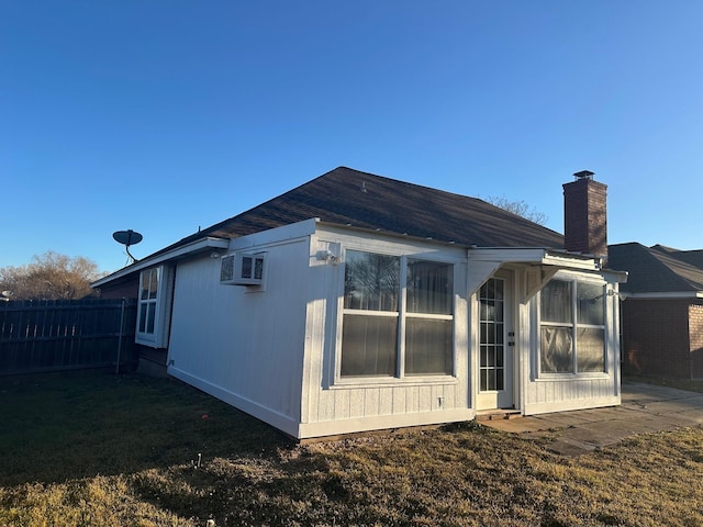 back of house with a chimney, a wall unit AC, fence, and a lawn