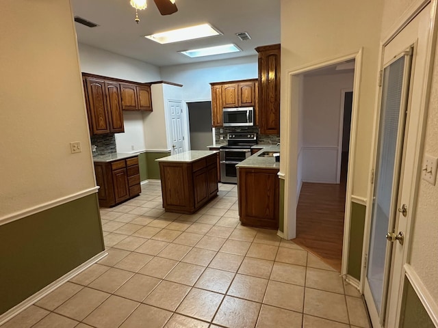 kitchen with light tile patterned floors, a kitchen island, ceiling fan, stainless steel appliances, and backsplash