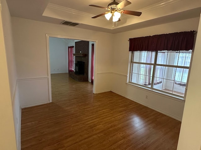 empty room with a raised ceiling, crown molding, ceiling fan, and dark hardwood / wood-style flooring