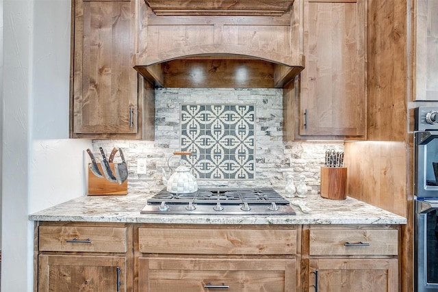 kitchen featuring decorative backsplash, custom exhaust hood, exhaust hood, light stone counters, and stainless steel appliances