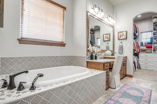 bathroom featuring a relaxing tiled tub and vanity