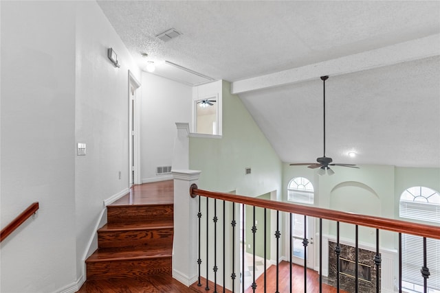 stairs with wood-type flooring, a textured ceiling, ceiling fan, a fireplace, and high vaulted ceiling