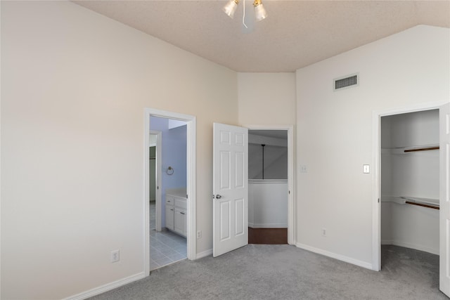 unfurnished bedroom with vaulted ceiling, a walk in closet, light colored carpet, and a closet