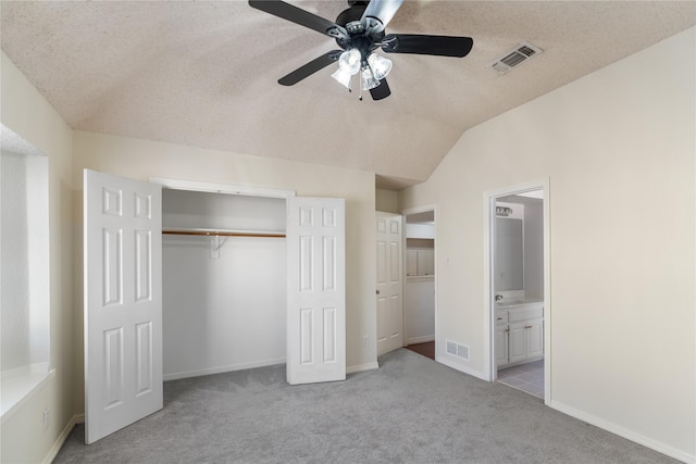 unfurnished bedroom featuring a closet, a textured ceiling, connected bathroom, lofted ceiling, and light colored carpet