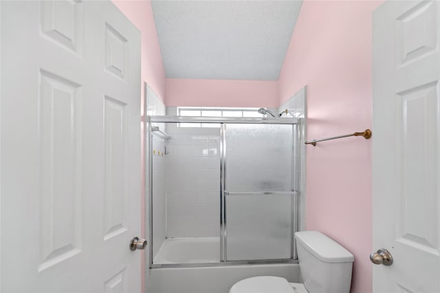 bathroom with shower / bath combination with glass door, a textured ceiling, and toilet