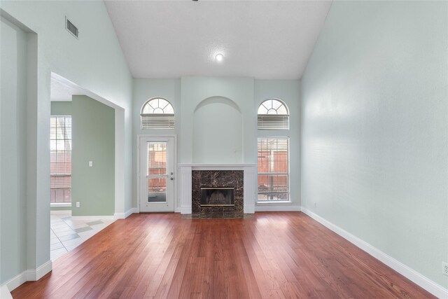 unfurnished living room featuring hardwood / wood-style flooring, a premium fireplace, plenty of natural light, and high vaulted ceiling