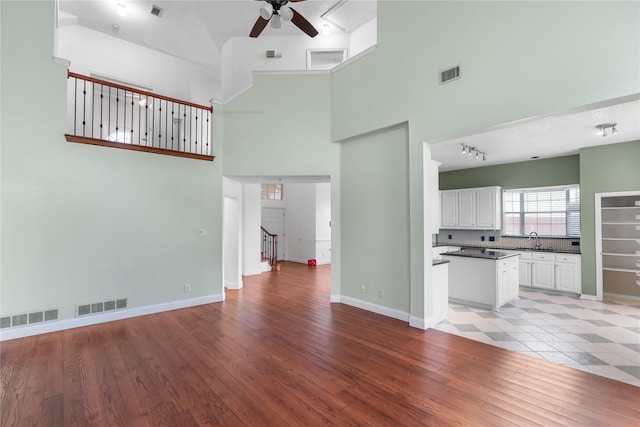 unfurnished living room with a high ceiling, sink, ceiling fan, and light hardwood / wood-style flooring