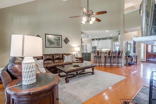 living room with crown molding, wood-type flooring, ceiling fan, and a towering ceiling