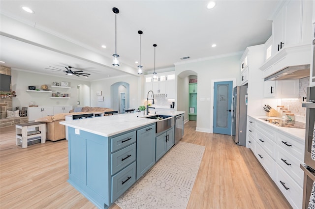 kitchen with sink, appliances with stainless steel finishes, a kitchen island with sink, white cabinets, and decorative light fixtures