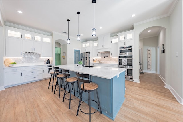 kitchen featuring pendant lighting, white cabinets, ornamental molding, a kitchen island with sink, and stainless steel appliances