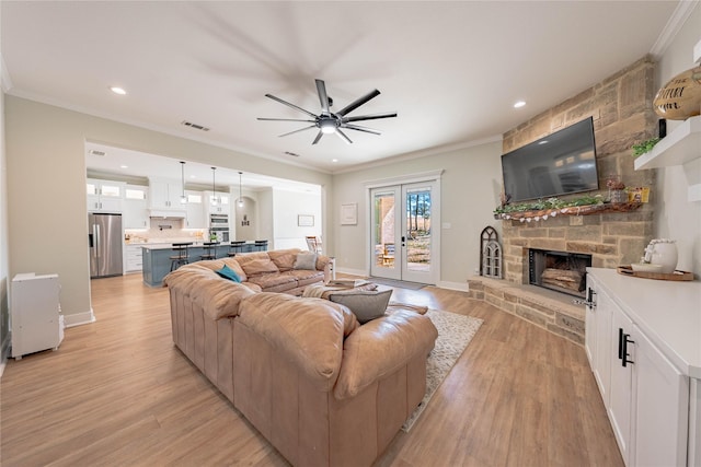 living room with french doors, ornamental molding, a stone fireplace, and light wood-type flooring