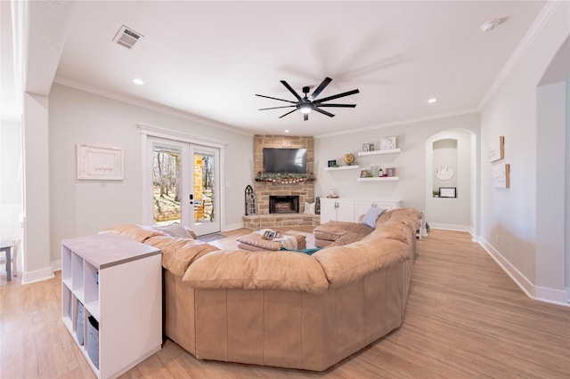 living room with a fireplace, light hardwood / wood-style flooring, ornamental molding, ceiling fan, and french doors