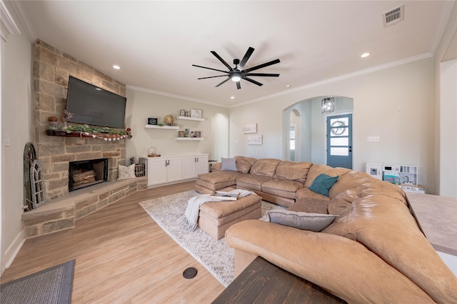 living room featuring a stone fireplace, ornamental molding, and light wood-type flooring