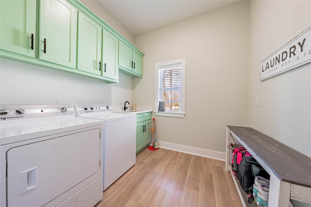 clothes washing area with sink, washer and clothes dryer, light hardwood / wood-style floors, and cabinets